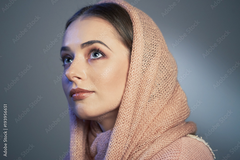 large emotional portrait of a beautiful girl in a knitted pink headscarf in the studio on a gray background. large emotional portrait of a beautiful girl in a knitted pink headscarf in the studio on a gray background.