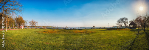 Spring on the lake Palic. People enjoy on beautiful spring afternoon walking near lake. Beautiful meadow with early spring flowers. Panoramic view.