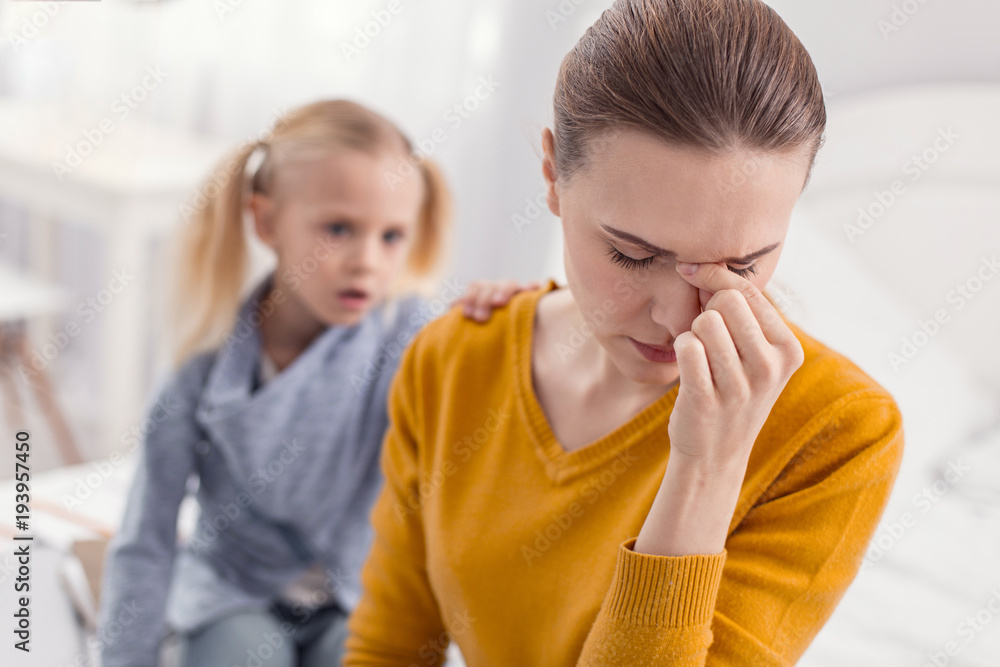 Not enough time. Young depressed attractive mother touching nose bridge while closing eyes and posing on the blurred background Not enough time. Young depressed attractive mother touching nose bridge while closing eyes and posing on the blurred background