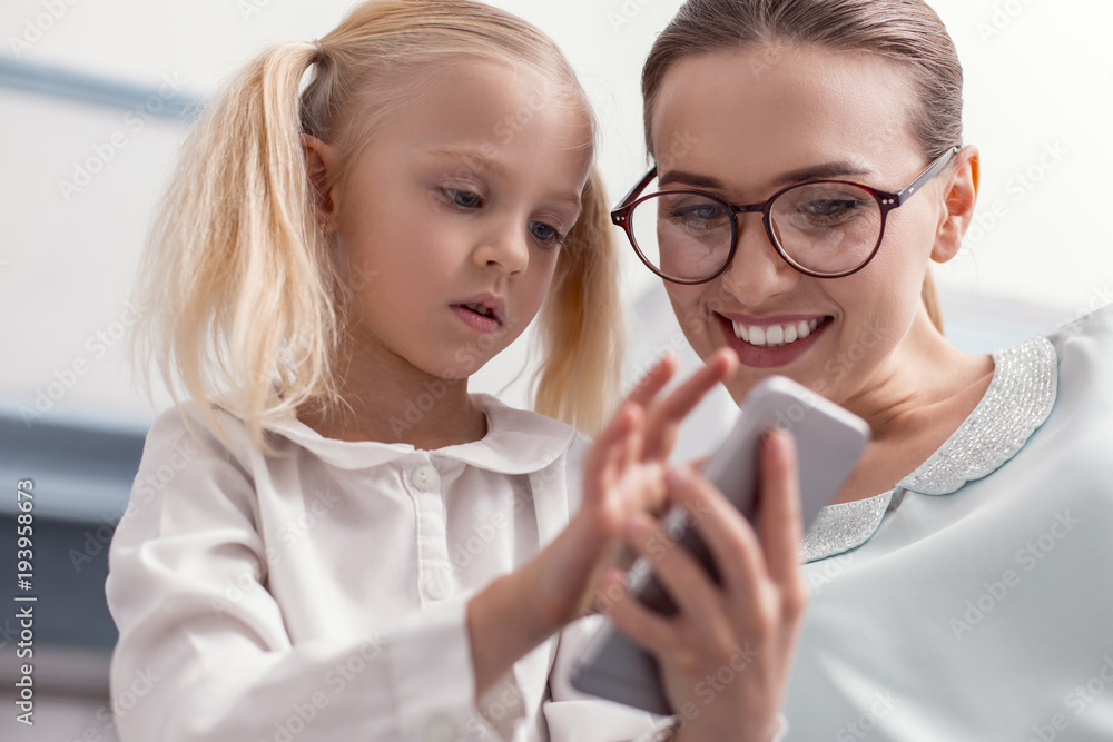 First time. Focused pretty girl touching phone while staring down and single mom helping her First time. Focused pretty girl touching phone while staring down and single mom helping her