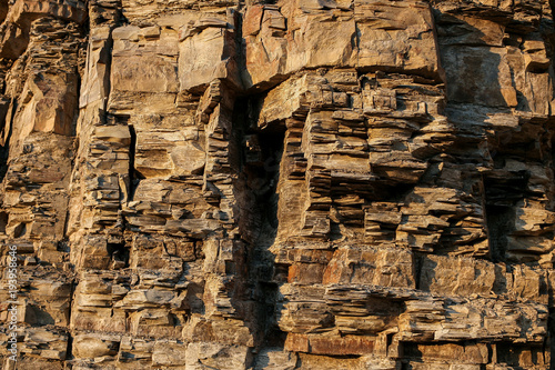 Close-up rufous stony wall with layered uneven hollowed-out surface. photo