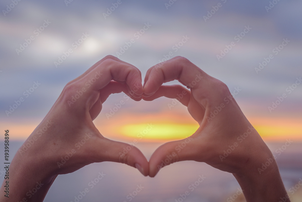 Bright sunset and hands of a man forming a heart shape silhouette on natural oudoors abstract background. Close up on emotional human feeling, over sunny seascape shore leisure travel landscape Bright sunset and hands of a man forming a heart shape silhouette on natural oudoors abstract background. Close up on emotional human feeling, over sunny seascape shore leisure travel landscape