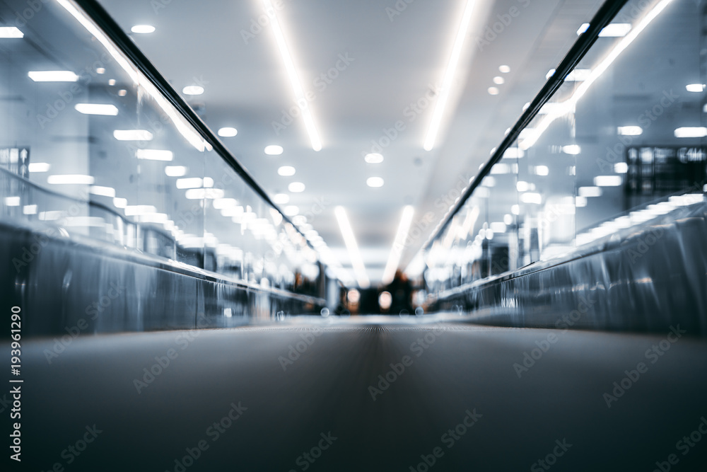 Fototapeta premium Shooting with very shallow depth of field of moving walkway in bright airport terminal interior; travelator trough contemporary departure area of railway station depot
