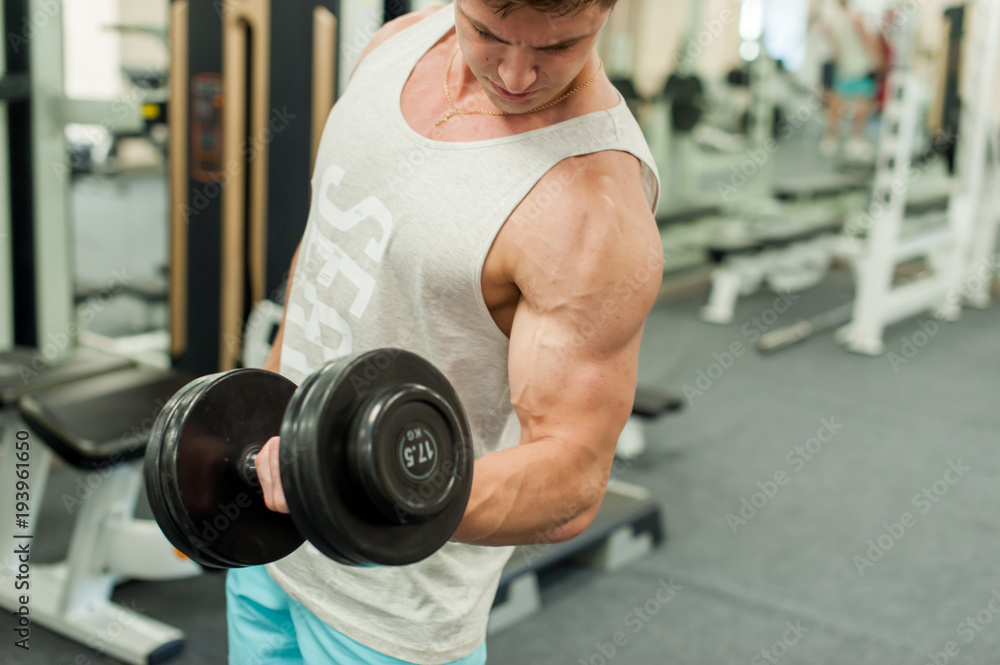 Young sexy male bodybuilder athlete, trains in the gym, using sports equipment and fitness equipment to improving health and beauty of the body Young sexy male bodybuilder athlete, trains in the gym, using sports equipment and fitness equipment to improving health and beauty of the body