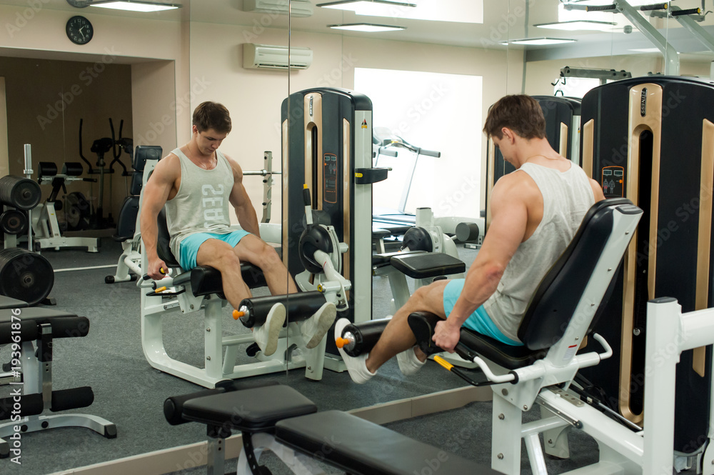 Young sexy male bodybuilder athlete, trains in the gym, using sports equipment and fitness equipment to improving health and beauty of the body Young sexy male bodybuilder athlete, trains in the gym, using sports equipment and fitness equipment to improving health and beauty of the body