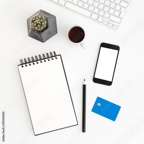 White office desk with spiral notebook, credit card, cactus and smartphone for mock up or product montage. Internet payment concept. Flat lay
