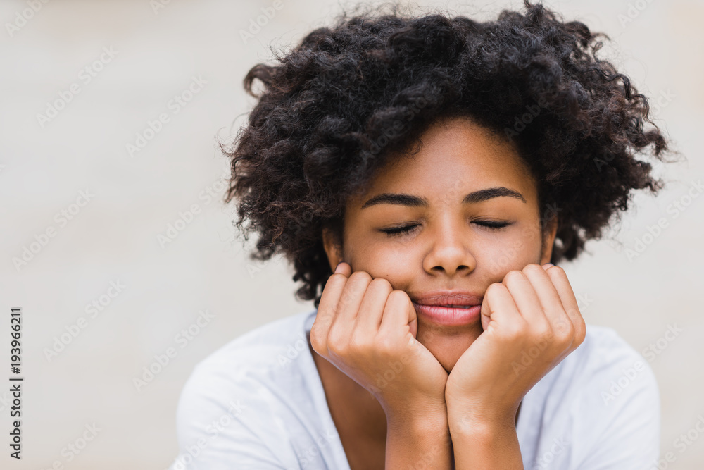 Pretty beautiful young woman with dark skin touching her chin and keeping eyes closed while feeling joyful and excited about something good happened, dressed casual. Lifestyle and people concept. Pretty beautiful young woman with dark skin touching her chin and keeping eyes closed while feeling joyful and excited about something good happened, dressed casual. Lifestyle and people concept.
