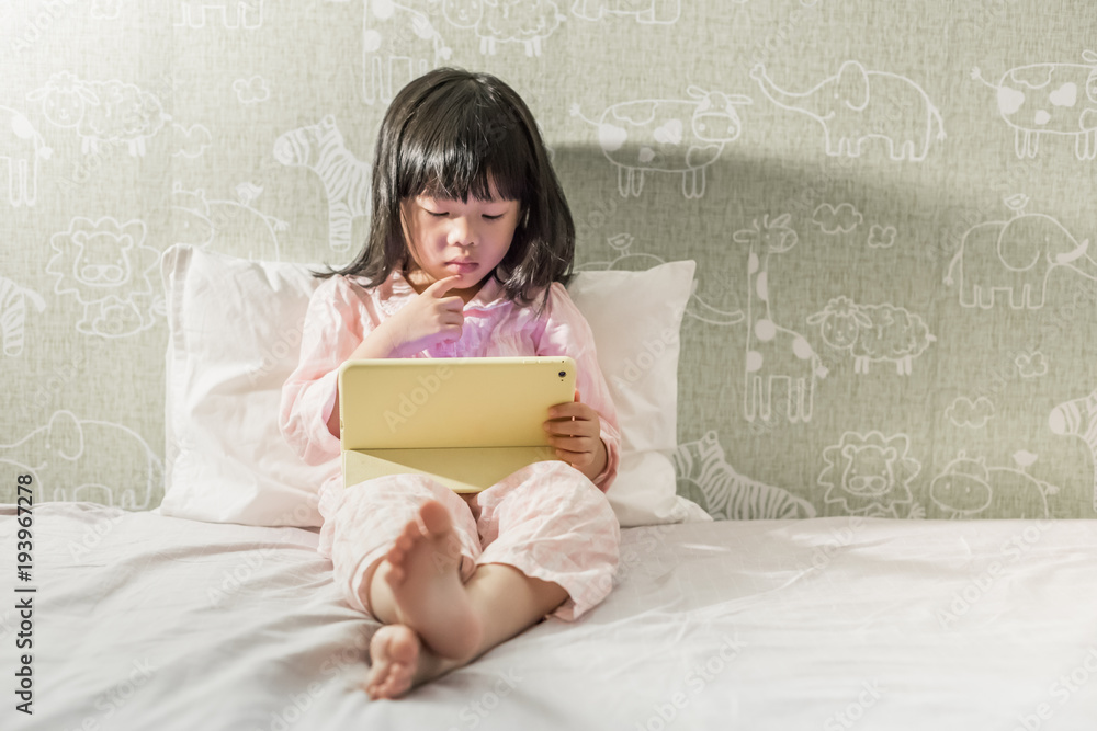 young little girl in pyjamas playing tablet on the bed young little girl in pyjamas playing tablet on the bed