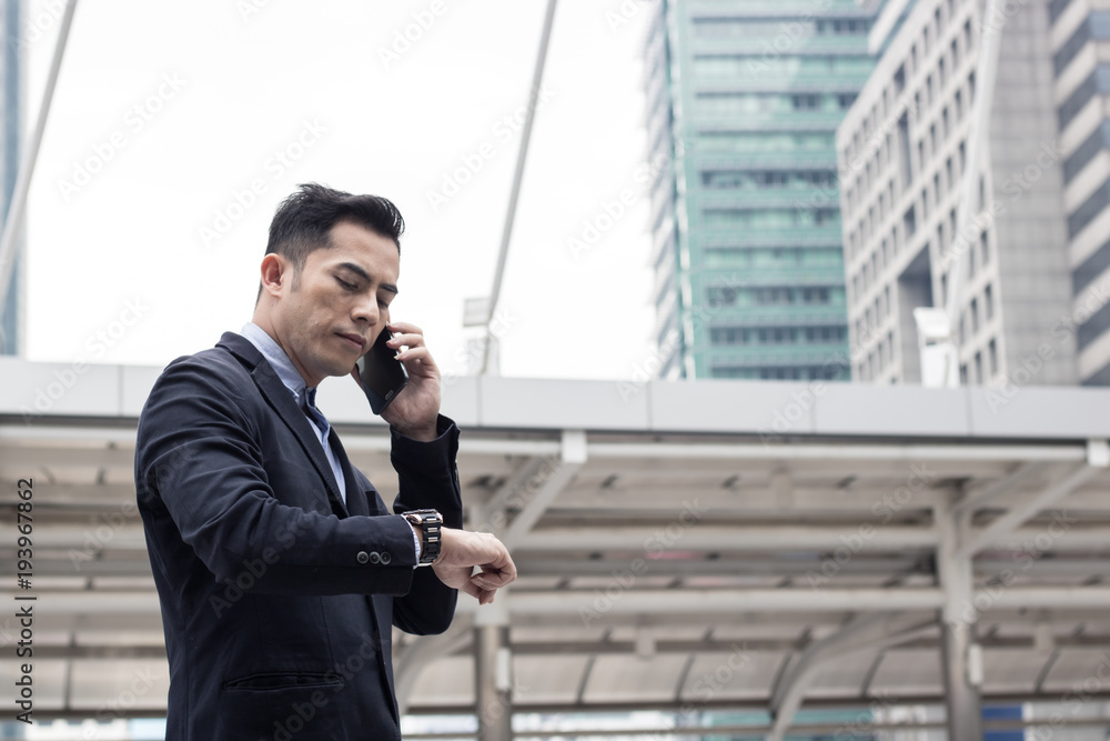 Businessman calling phone outside of building for connection and communication and watching watch. Businessman calling phone outside of building for connection and communication and watching watch.