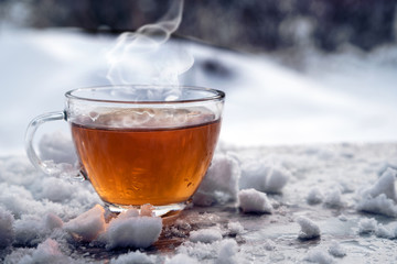 steaming hot tea in a glass cup is standing outside on a cold winter day with snow, copy space
