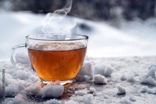 steaming hot tea in a glass cup is standing outside on a cold winter day with snow, copy space