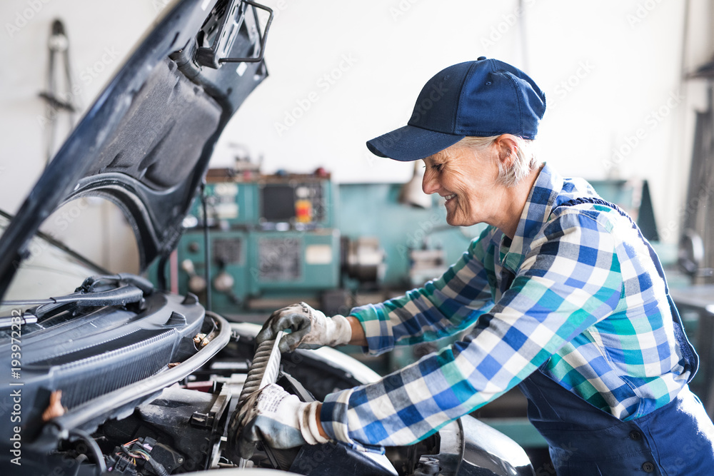 Senior female mechanic repairing a car in a garage.