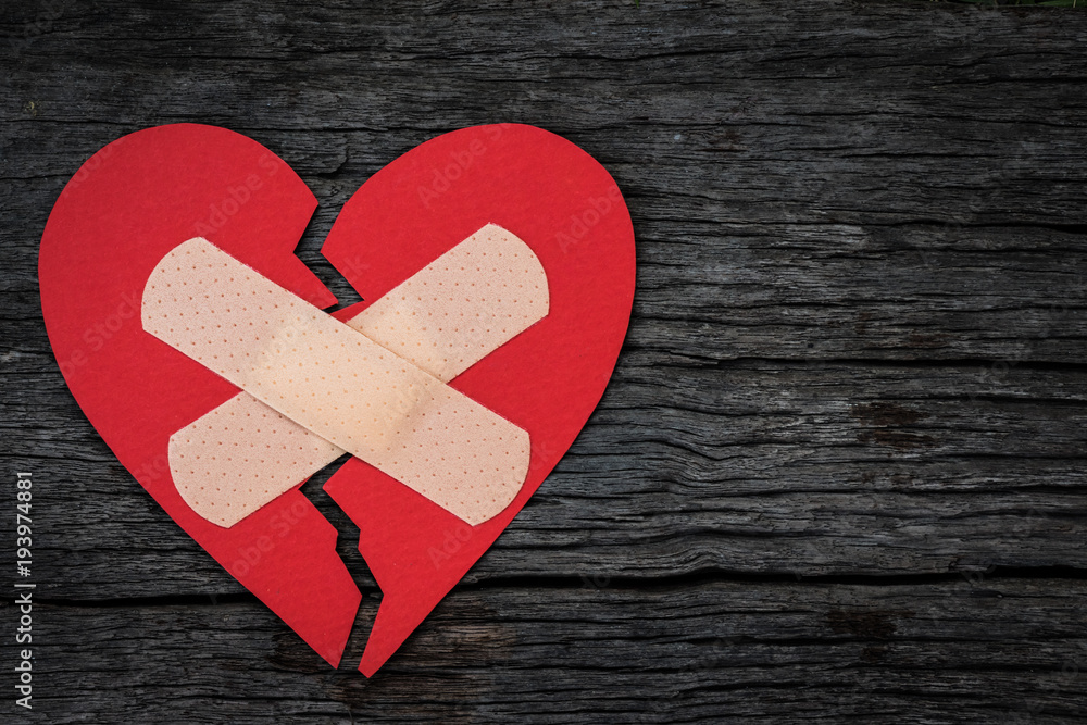 First Aid Band Cushioned Plaster Strip Medical Patch glued on red heart paper on wooden background. Heart broken, Love and Valentines day concept. First Aid Band Cushioned Plaster Strip Medical Patch glued on red heart paper on wooden background. Heart broken, Love and Valentines day concept.