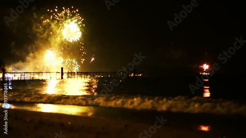 Bright golden fireworks explode in the night sky above the surface of the sea. On New Years's Eve colored lights are reflected in the ocean water. Holidays on the coast. Celebtarion with pyrotechnics photo