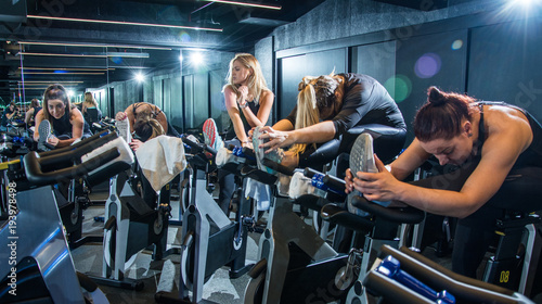 Group of young women in sportswear stretching their legs on exercise bikes before cycling class in health club.
