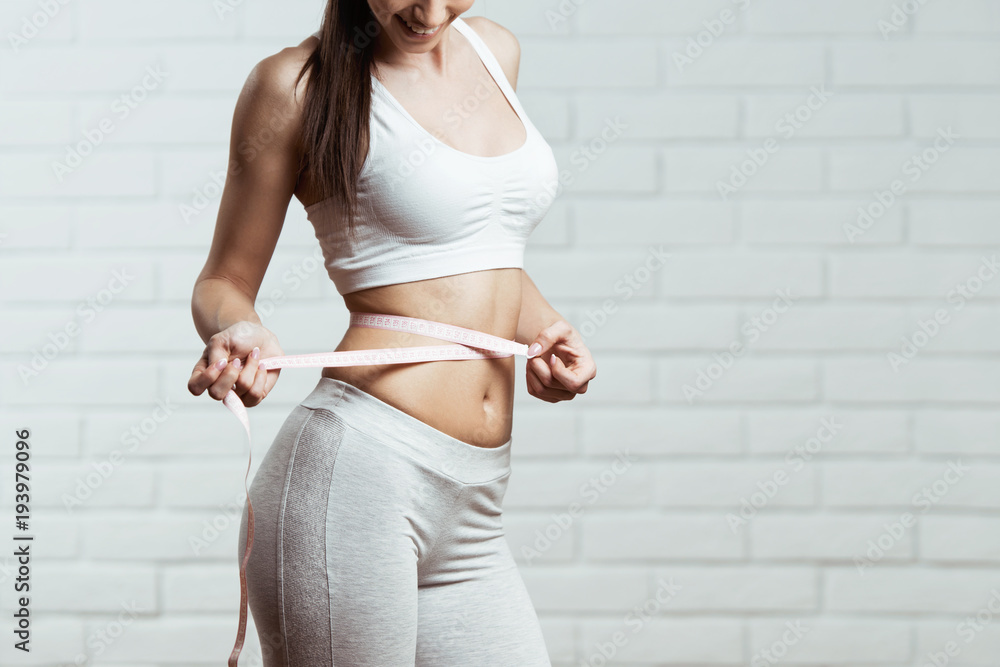 Beautiful, fit, young woman measuring her waist  - obrazy, fototapety, plakaty 
