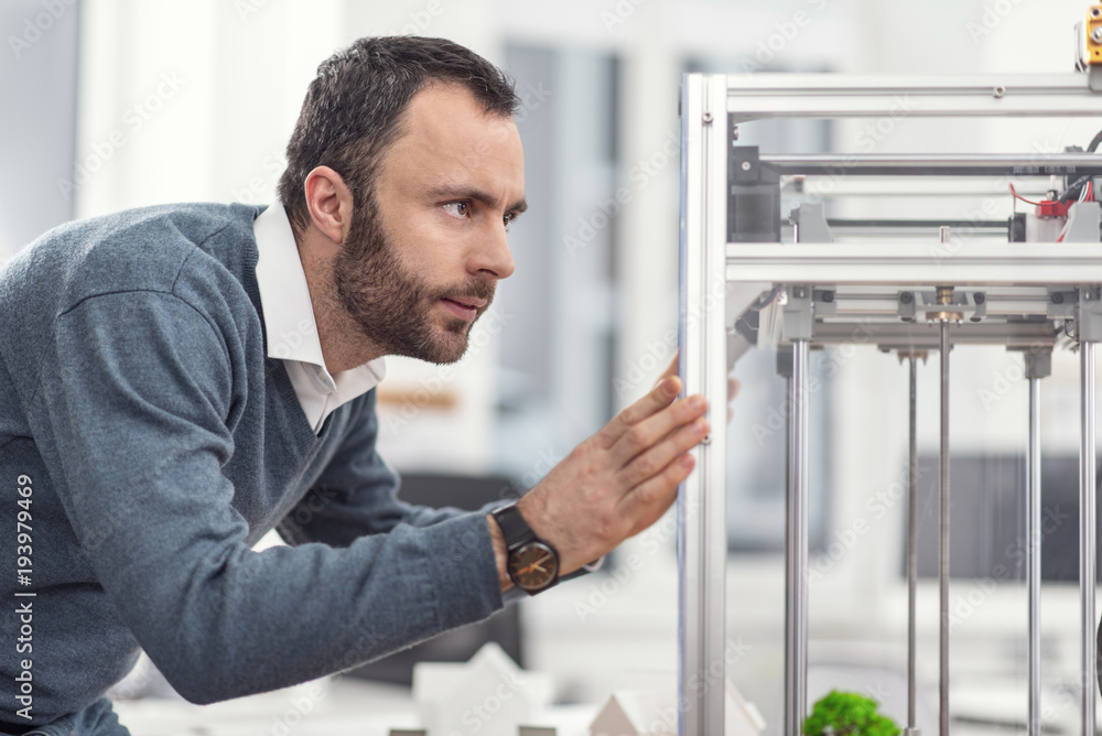 Delicate treatment. Bristled young engineer repositioning 3D printer, moving it with both hands while being careful not to harm the device Delicate treatment. Bristled young engineer repositioning 3D printer, moving it with both hands while being careful not to harm the device