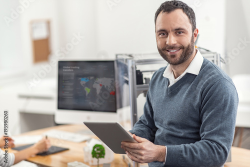 Wallpaper Mural New information. Joyful bristled young man leaning on the desk in the office and posing for the camera while reading from tablet new data regarding his project Torontodigital.ca
