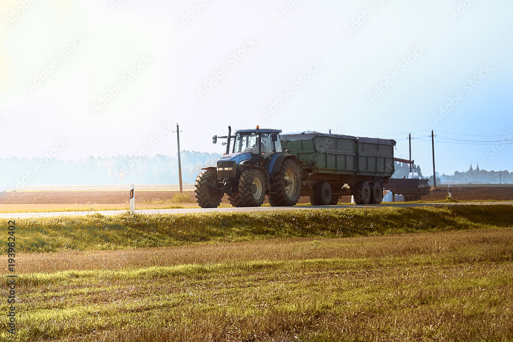 Fototapeta premium Tractor rides on the asphalt road in the sunlight