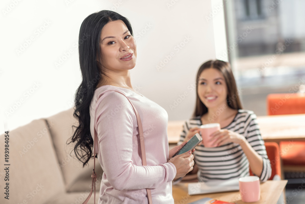 Pleasant communication. Positive nice delighted woman standing behind her friend and talking to her while discussing latest news Pleasant communication. Positive nice delighted woman standing behind her friend and talking to her while discussing latest news