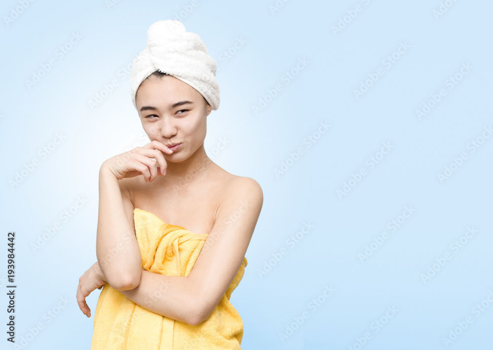 Funny portrait of cheerful smiling attractive asian woman holding white towel on head wrapped in yellow towel isolated on the blue background. Beauty, skincare, lifestyle concept