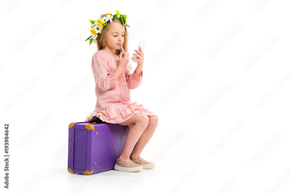 Side view of kid sitting on purple suitcase and doing makeup by lipstick isolated on white Side view of kid sitting on purple suitcase and doing makeup by lipstick isolated on white