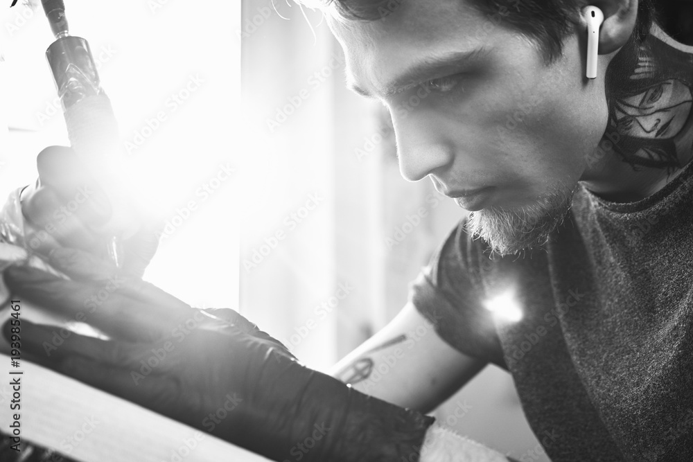 A young guy, beats a tattoo on the hand of the girl in a tattoo parlor, rotary tattoo machine, black ink, lens flare