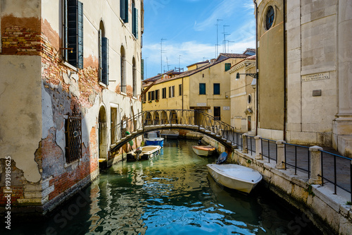 An old canal in Venice with parked boats and a small pedestrian bridge