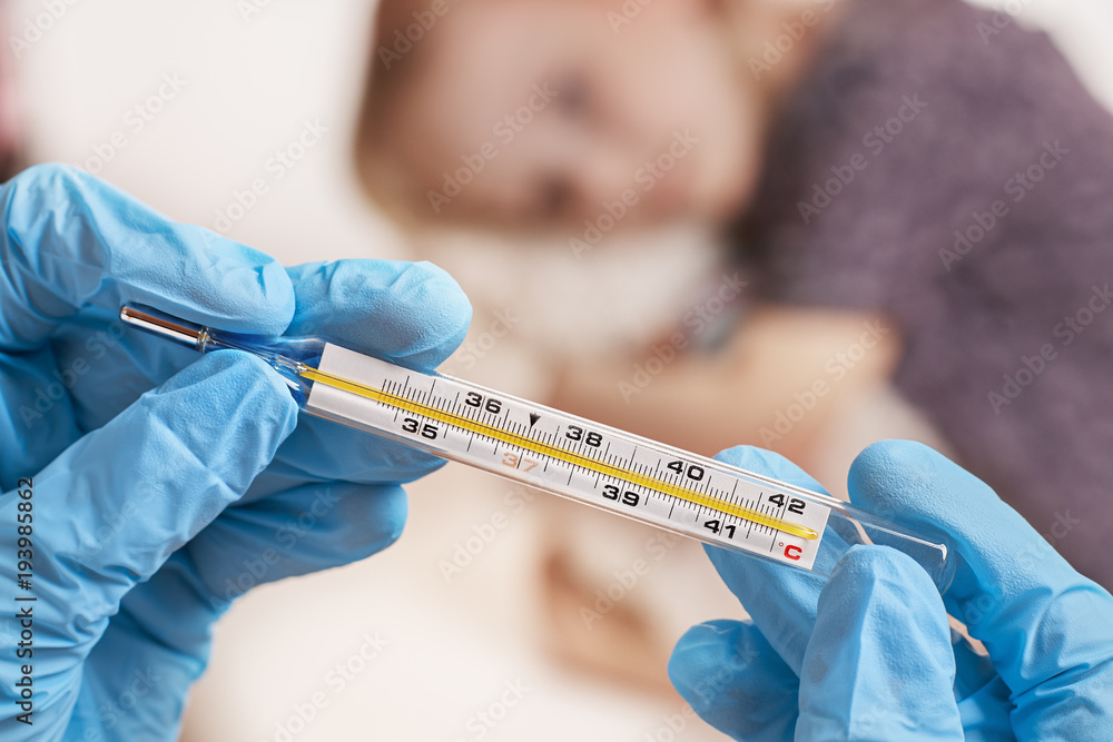 Close Up shot at a thermometer. Hands in medical gloves hold a mercury thermometer. A little girl is measured by temperature. Shallow depth of field with a focus on the thermometer. Close Up shot at a thermometer. Hands in medical gloves hold a mercury thermometer. A little girl is measured by temperature. Shallow depth of field with a focus on the thermometer.