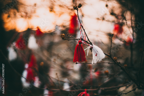 Red and white beautiful martisor hanging on the branches of the tree in the evening At the sunset