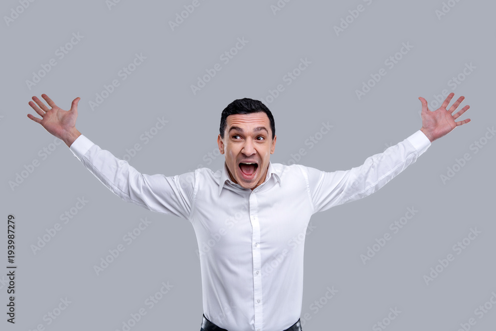 Overwhelmed with feelings. Handsome exuberant dark-eyed young man wearing a white shirt and smiling and expressing his feelings of happiness Overwhelmed with feelings. Handsome exuberant dark-eyed young man wearing a white shirt and smiling and expressing his feelings of happiness