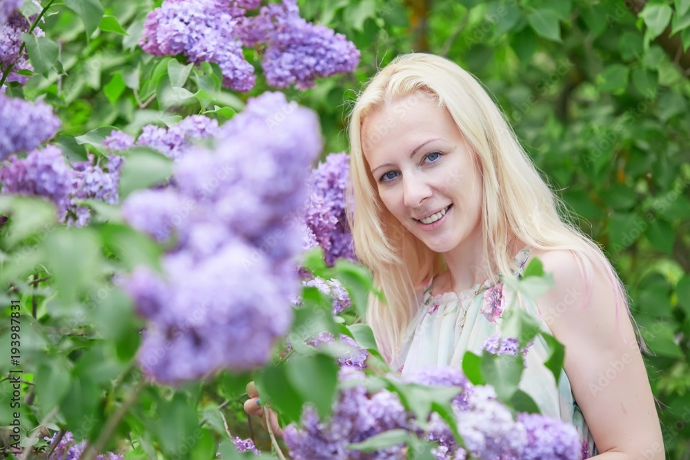 Young blonde woman standing in a spring blooming garden. Fashion Romantic girl outdoors portrait in blooming trees. Young blonde woman standing in a spring blooming garden. Fashion Romantic girl outdoors portrait in blooming trees.