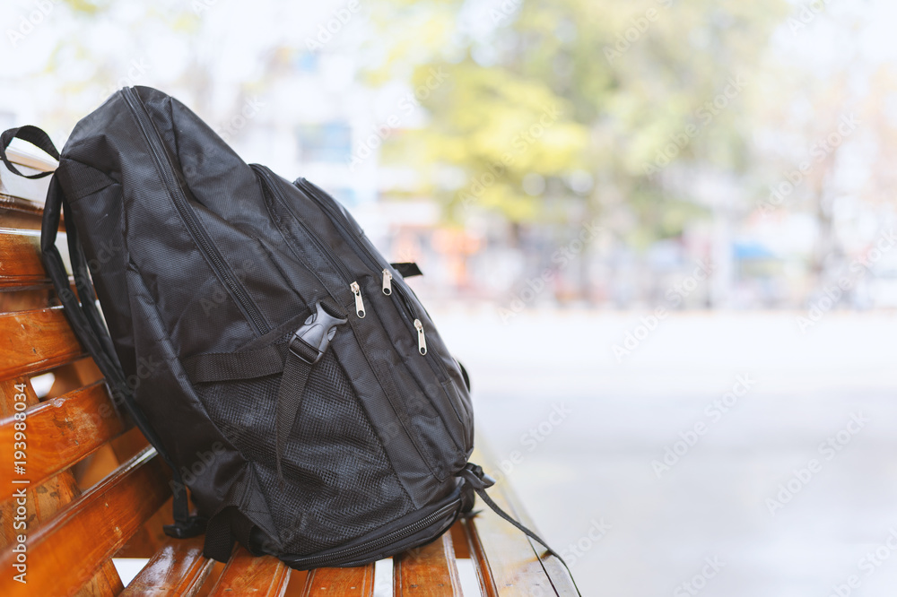 black backpack on wooden table in bus stations with soft-focus and over light in the background - obrazy, fototapety, plakaty 