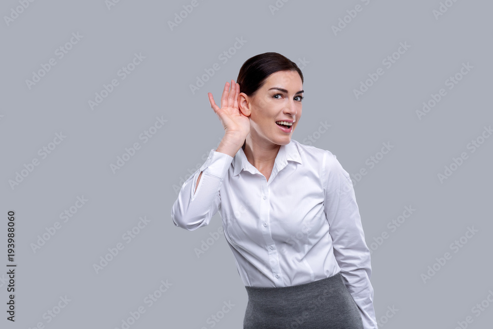 Smiling. Beautiful happy dark-eyed young businesswoman wearing a white shirt and smiling and having her hand near her ear Smiling. Beautiful happy dark-eyed young businesswoman wearing a white shirt and smiling and having her hand near her ear
