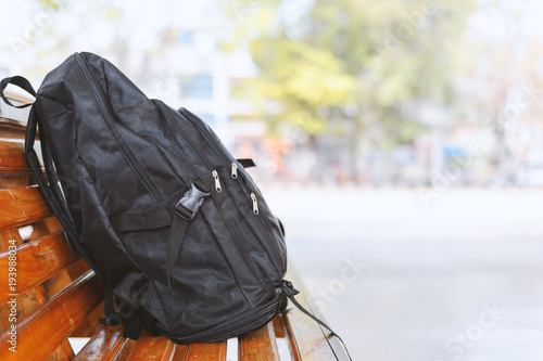 black backpack on wooden table in bus stations with soft-focus and over light in the background