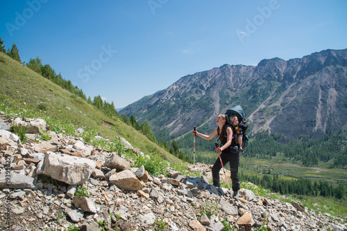 Woman Hiker trekking in mountains with child in backpack . Mother with baby boy travelling in summer sunny day.
