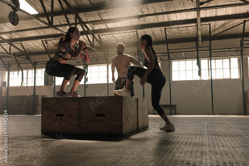Group of people doing box jumping workout in gym