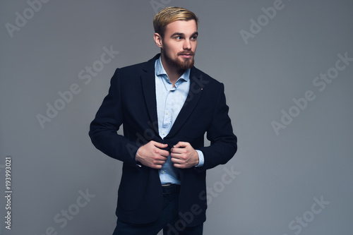 Professional and stylish. A portrait of a business man holding the lapels of his jacket in front of the grey background.