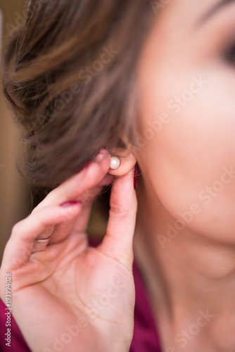 Bride puts on earrings with pearls in her ear. Delicate brunette touches her luxury earrings. Wedding details