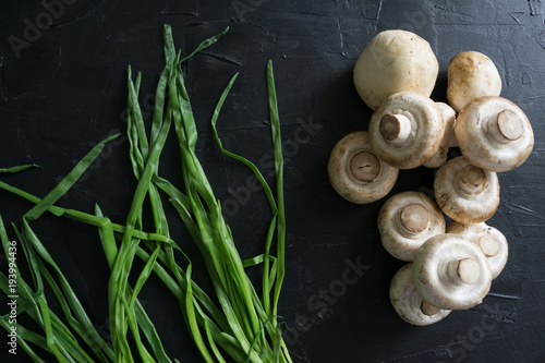 Raw champignons with green onion on black background top view