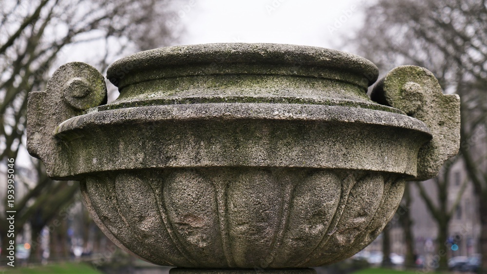 Fototapeta premium Stone jug slightly moss-covered, in the blurred background autumnal trees and house