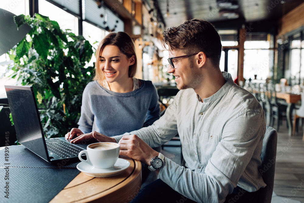 Cheerful man in eyeglasses and beautiful woman looking at laptop screen, while sitting at cafe. Time with pleasure. Cheerful man in eyeglasses and beautiful woman looking at laptop screen, while sitting at cafe. Time with pleasure.