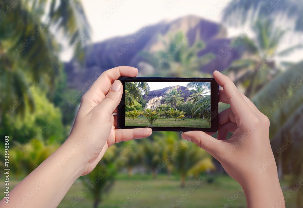 Female hand taking picture of La Digue island on mobile phone. Picture of Seychelles island on smart phone Female hand taking picture of La Digue island on mobile phone. Picture of Seychelles island on smart phone