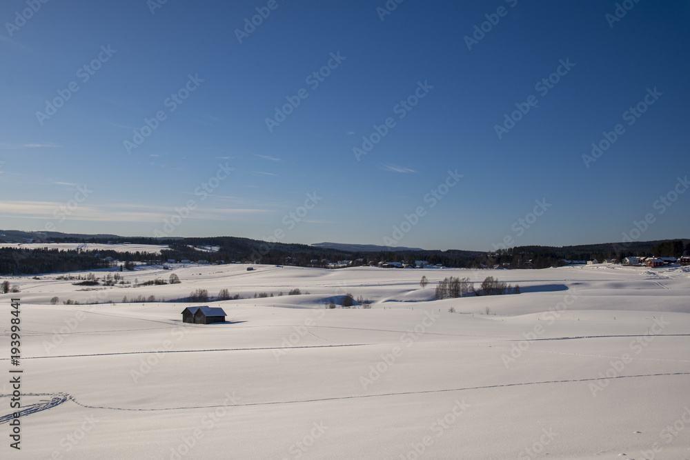 Snow covered field with some barns and a village in background