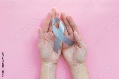 Parkinson's disease awareness or brain cancer grey bow or silver ribbon in woman or female hands over light pink background with copy space for text, logo, wordings decoration, health medical concept