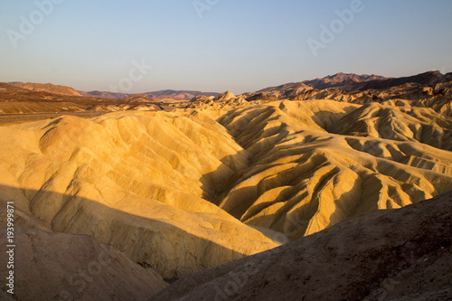 Setting sun on the eroded mountain ridges of desert dry and hot landscape at Zabriskie Point Death Valley National Park, California, evening time of sunny day before sunset