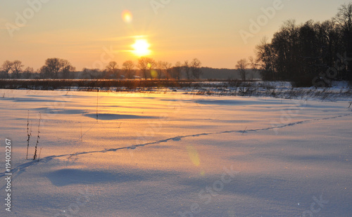 Solar lens flare sunset in winter frozen field landscape.