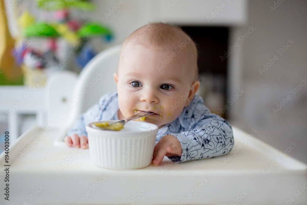 Cute little baby boy, eating mashed vegetables for lunch, mom feeding him Cute little baby boy, eating mashed vegetables for lunch, mom feeding him
