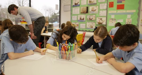 4K Young school children working in groups in classroom with teacher helping out in background. Slow motion