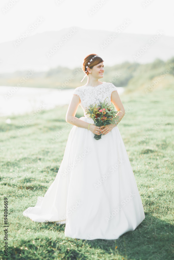 Fototapeta premium Bride in wedding dress posing on grass with beautiful landscape background